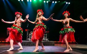 3 ladies in Hawaiian attire dancing on stage