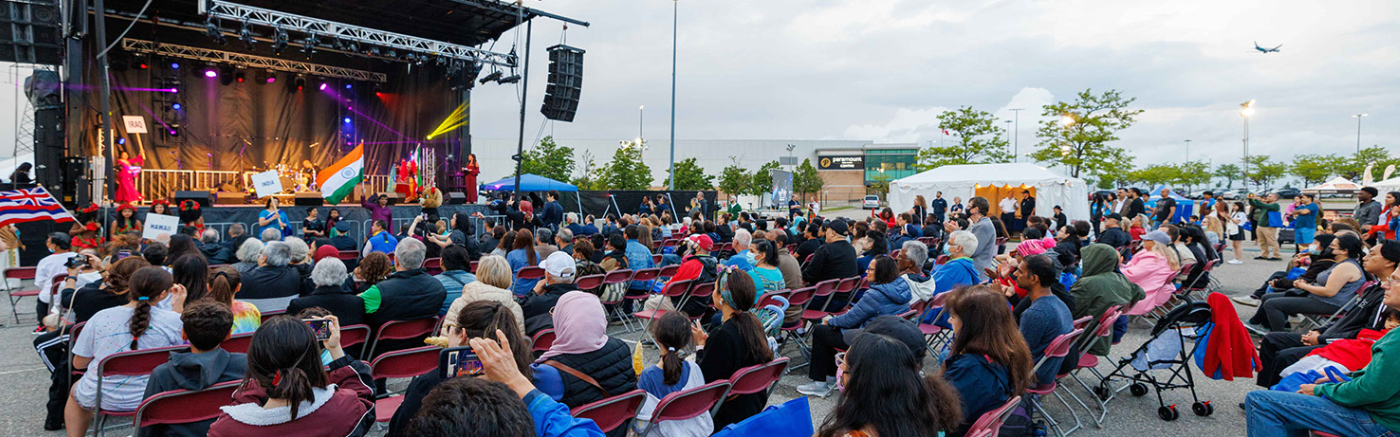 Group of individuals sitting in chairs outdoors infront of a stage watching a performance